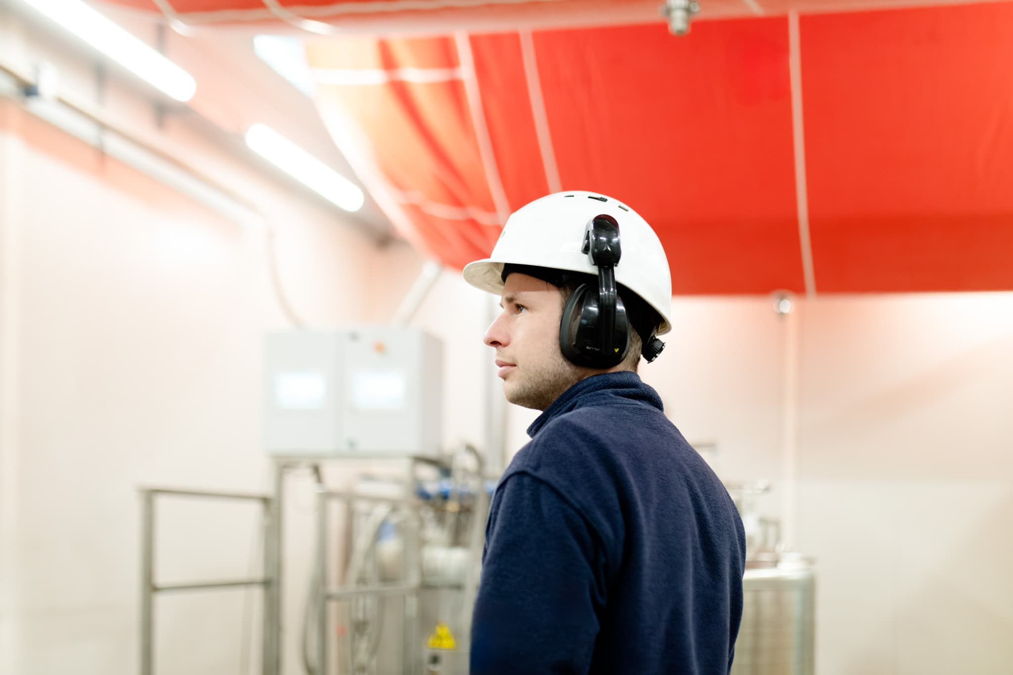 Industrial worker wearing a white safety helmet and earmuffs inside a factory setting