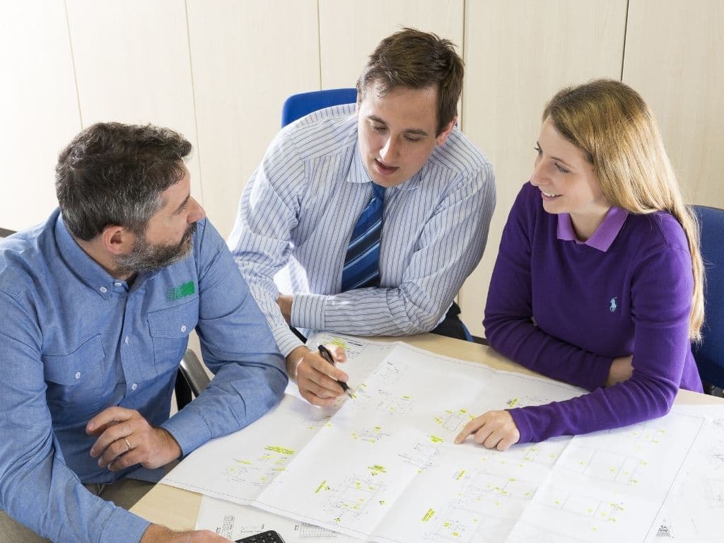Three colleagues reviewing technical drawings and plans during a project meeting