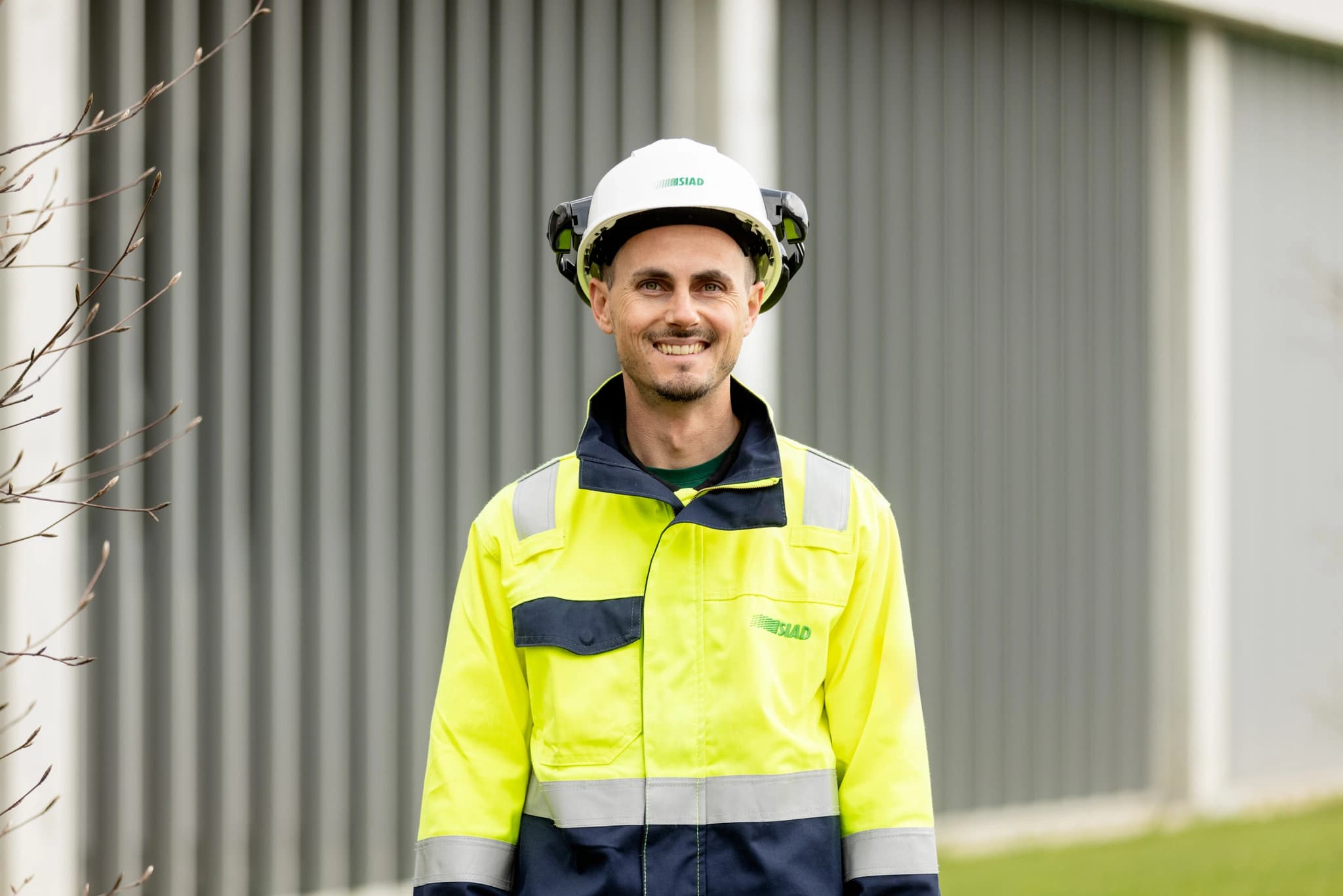 SIAD employee smiling with safety helmet and vest in front of the Gases of Life District