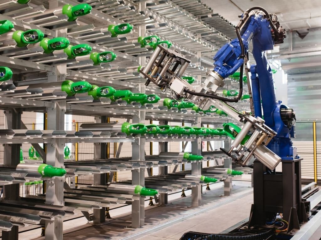 Blue industrial robotic arm handling green components on automated storage racks in factory