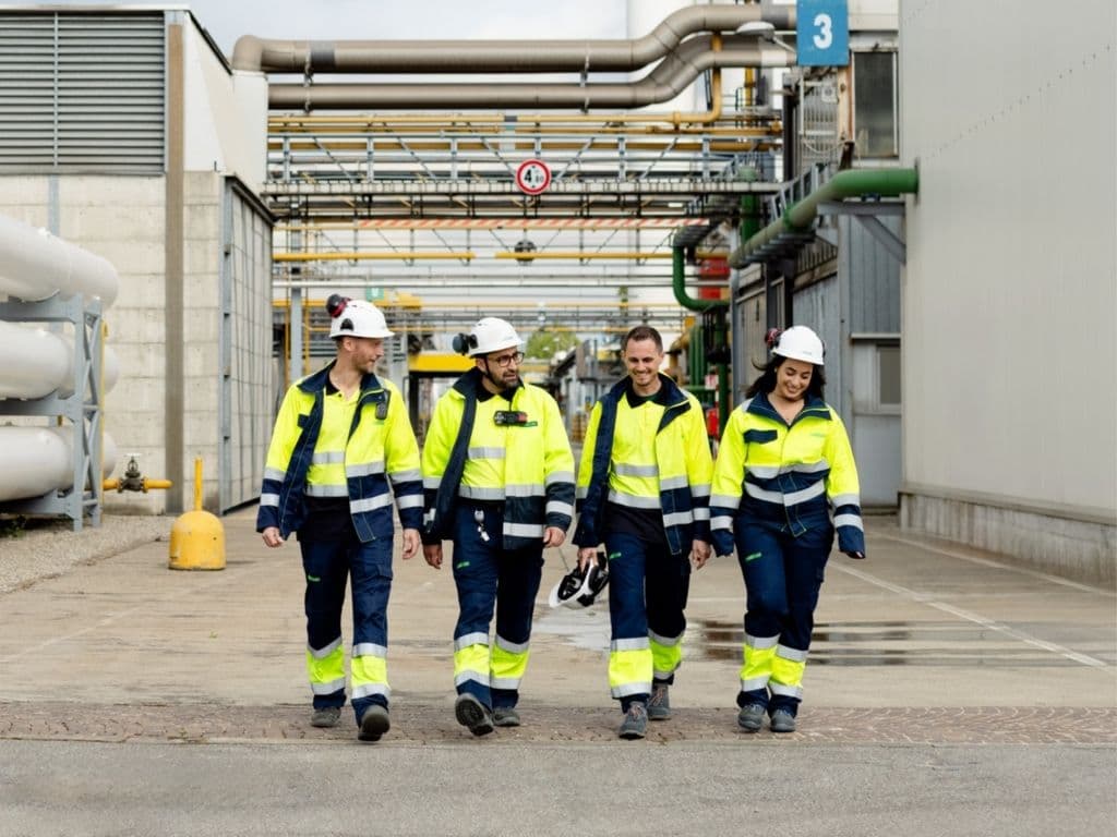 Industrial workers in high-visibility safety gear walking through a gas plant facility